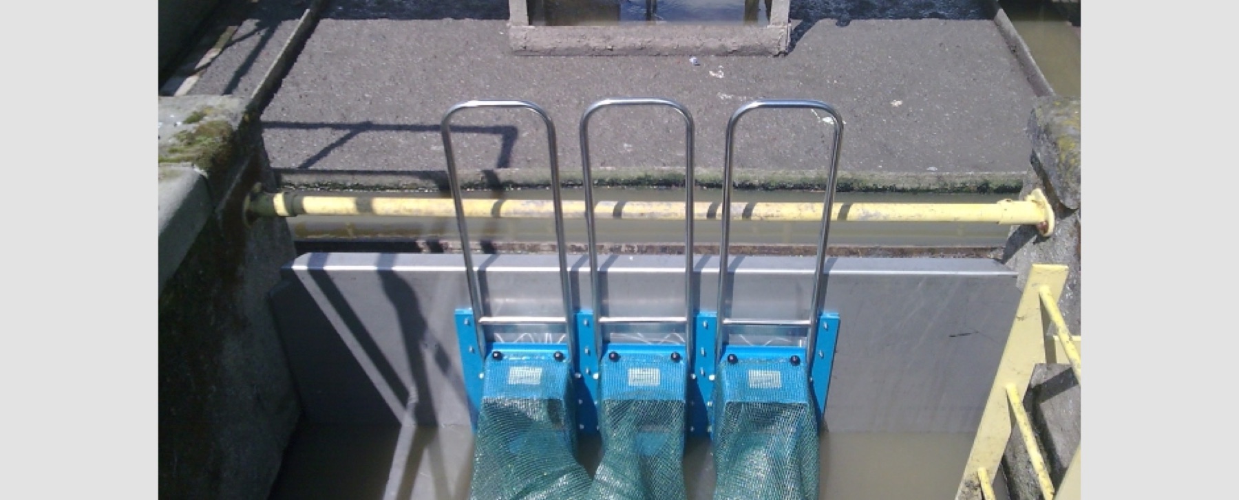 Three stainless steel penstock screens set in a concrete channel