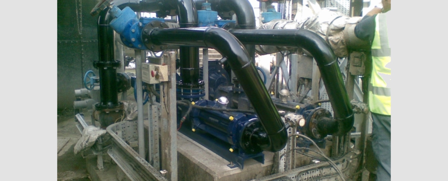 A blue pump set with black pipework and valves in a plant room